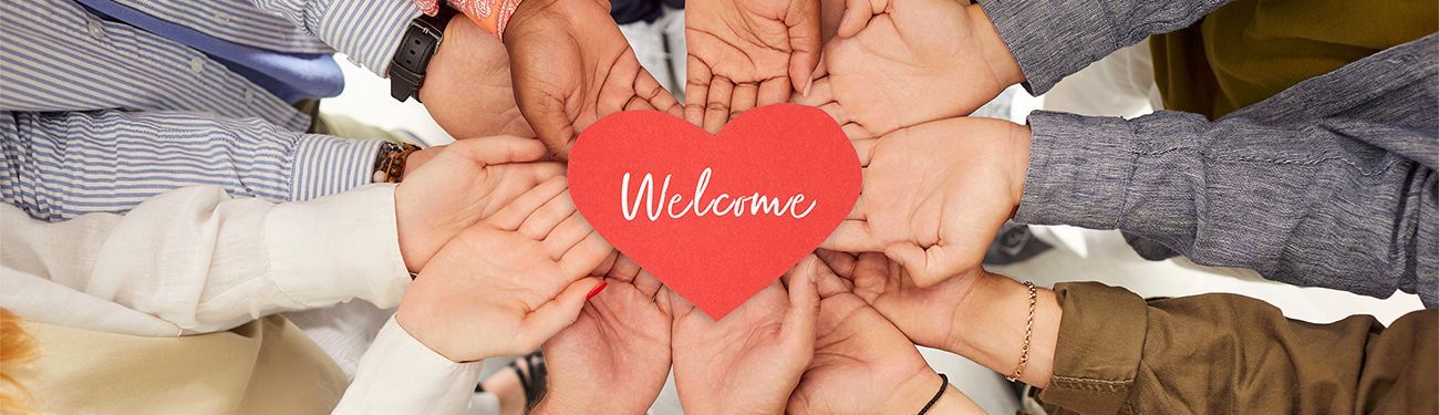 A group of people are holding a red heart in their hands that says welcome.