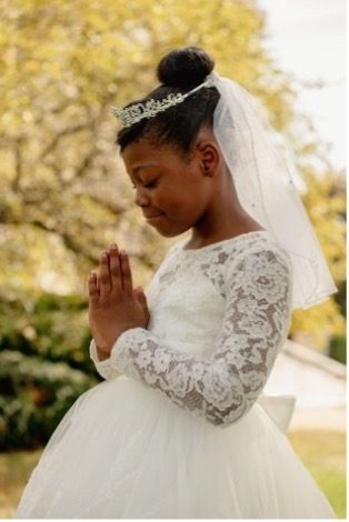 A little girl in a white dress and veil is praying.