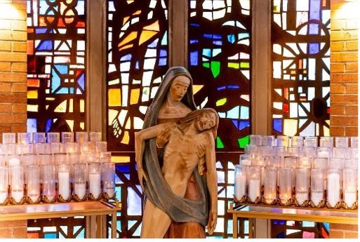 A statue of a woman holding jesus in front of a stained glass window.