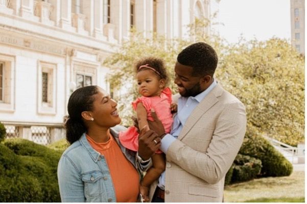 A man and woman are holding a baby in front of a building.