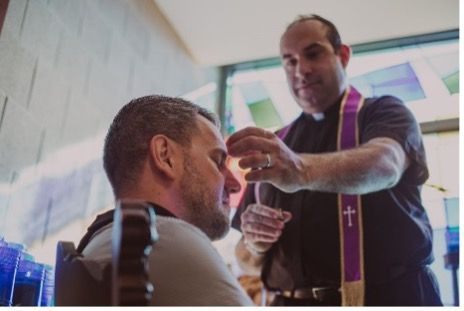 A priest who is standing offering a blessing to a man who is sitting down.