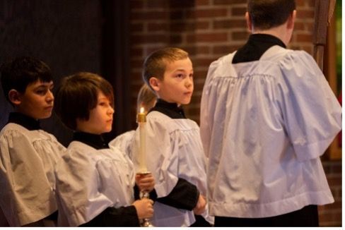 A group of young boys in white robes are holding candles in a church.