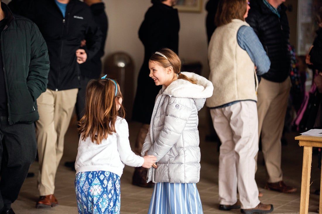 Two little girls are holding hands in a crowd of people.