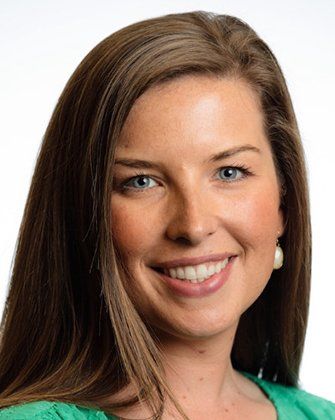 A woman with long brown hair is smiling and wearing a green shirt.