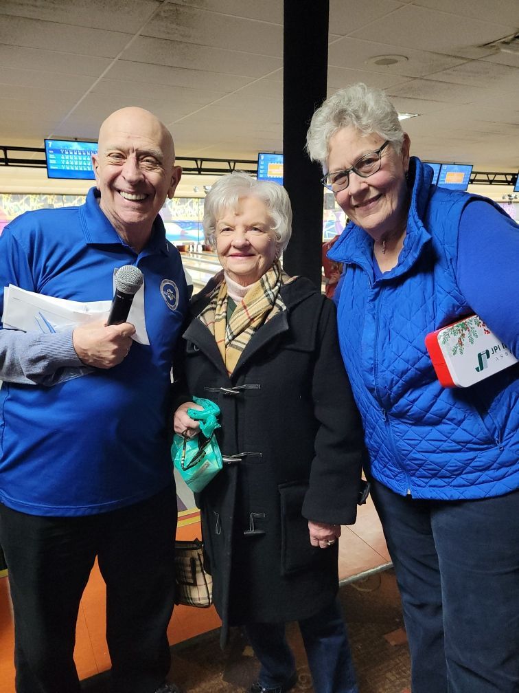 A man is holding a microphone and two women are standing next to each other in a bowling alley.