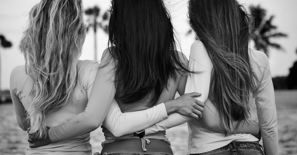 Three women are hugging each other on the beach in a black and white photo.