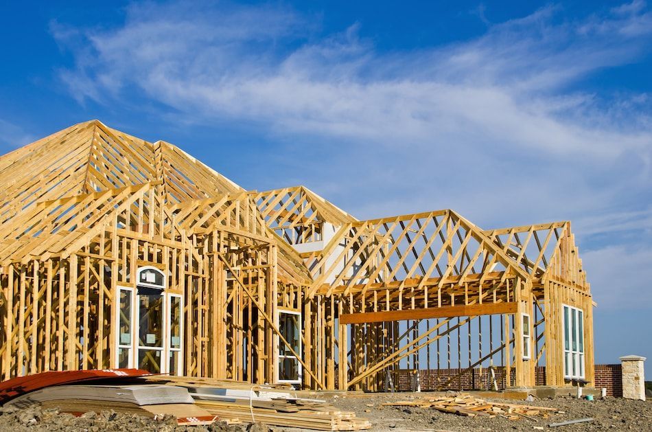 Framed wooden structure of a house under construction against a blue sky.