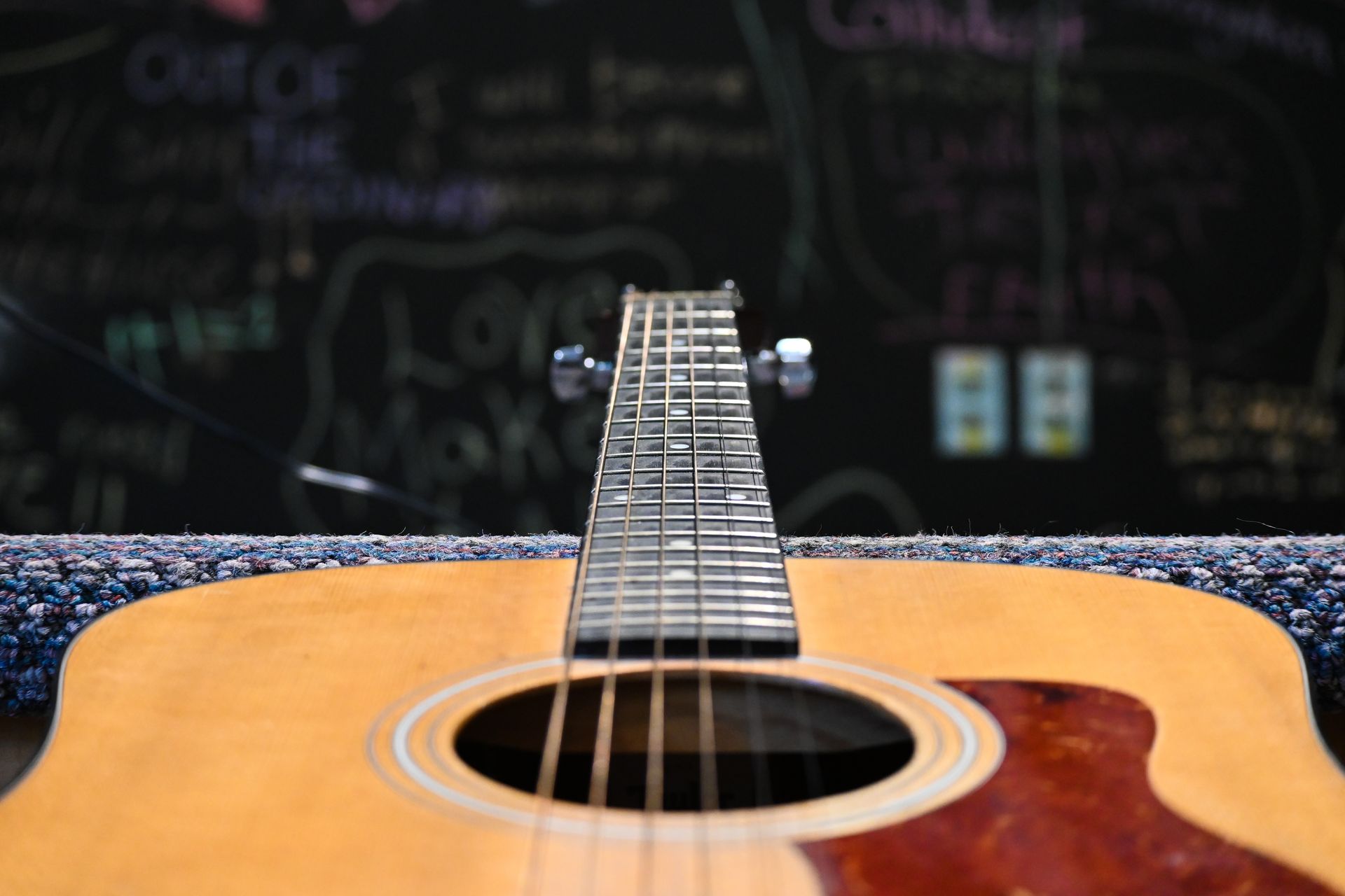 A close up of an acoustic guitar with a chalkboard in the background