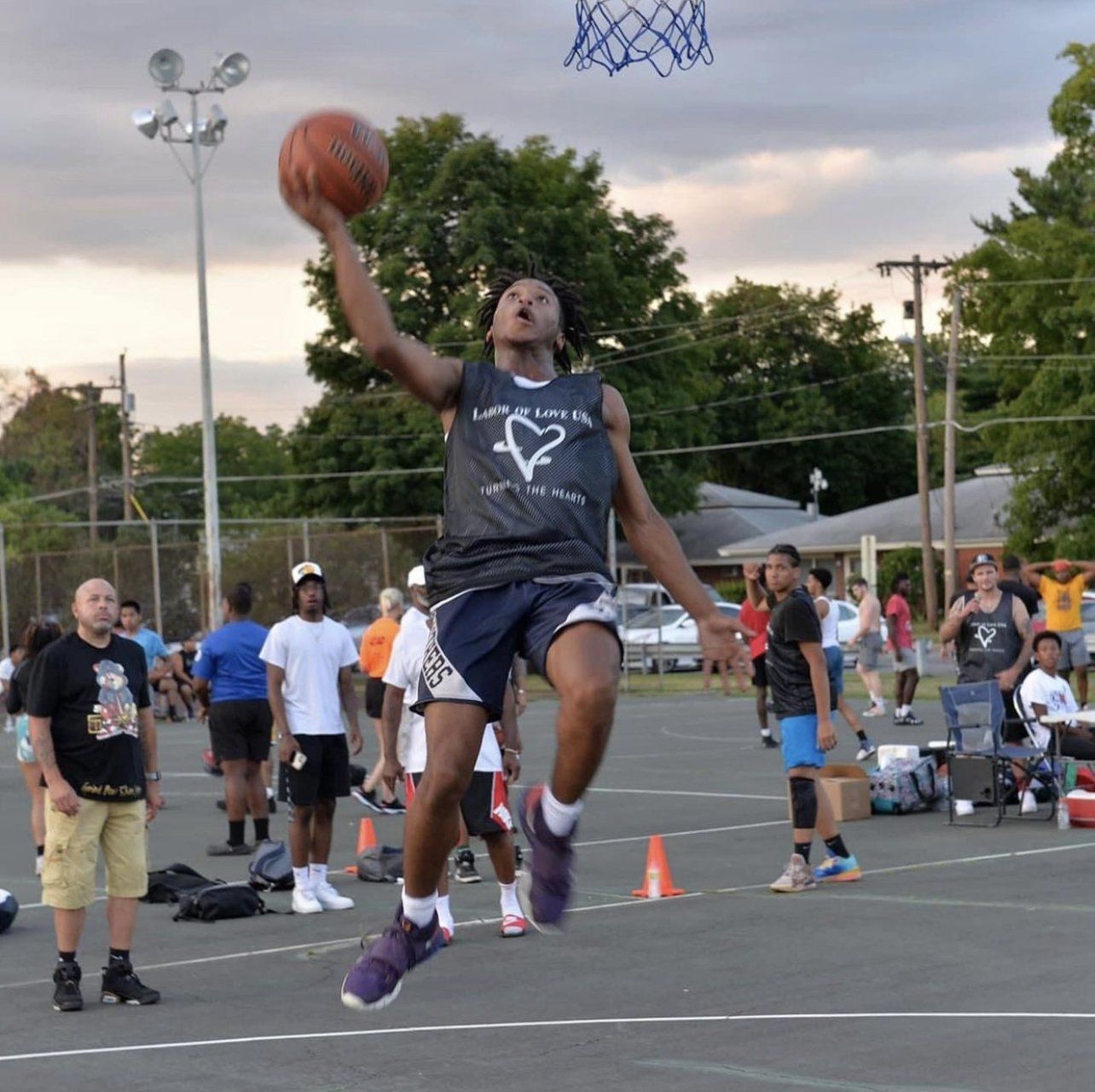 A man in a black tank top with a triangle on it is jumping in the air with a basketball