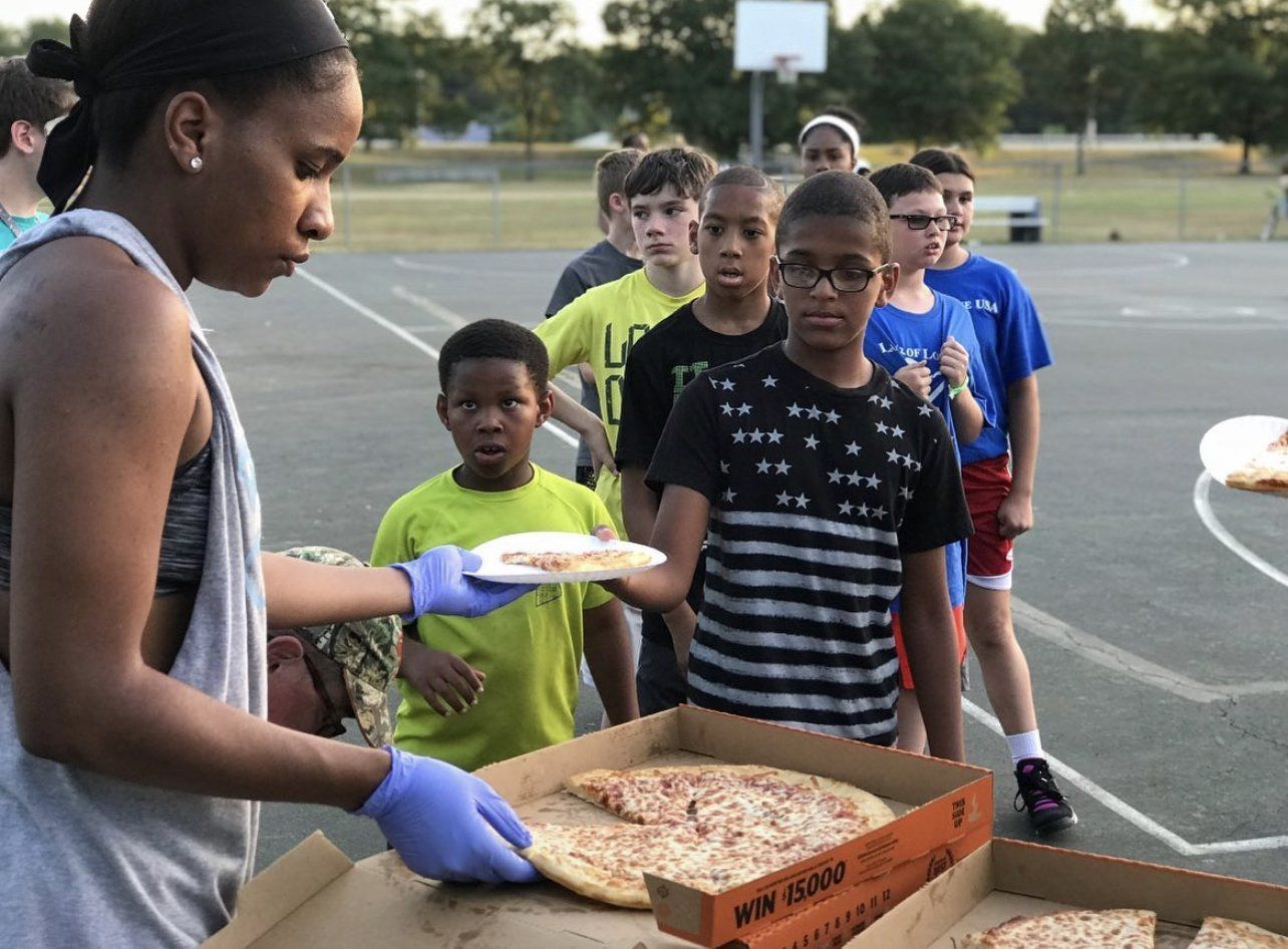 A girl is serving pizza to a group of children.
