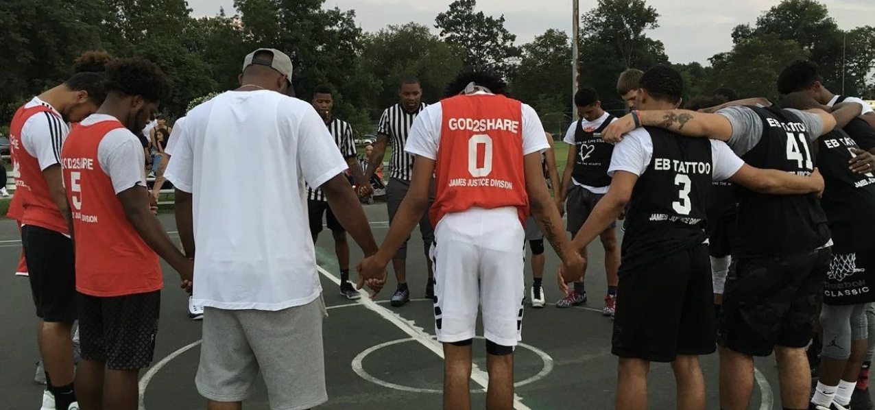 A group of young men are standing in a circle on a basketball court holding hands.