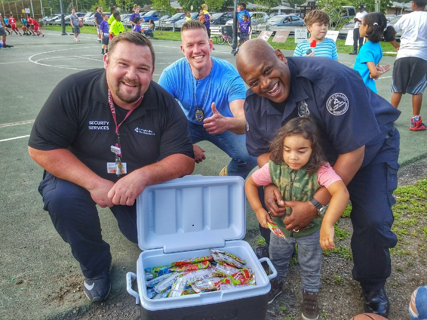 A group of men and a little girl are posing for a picture with a cooler full of candy.