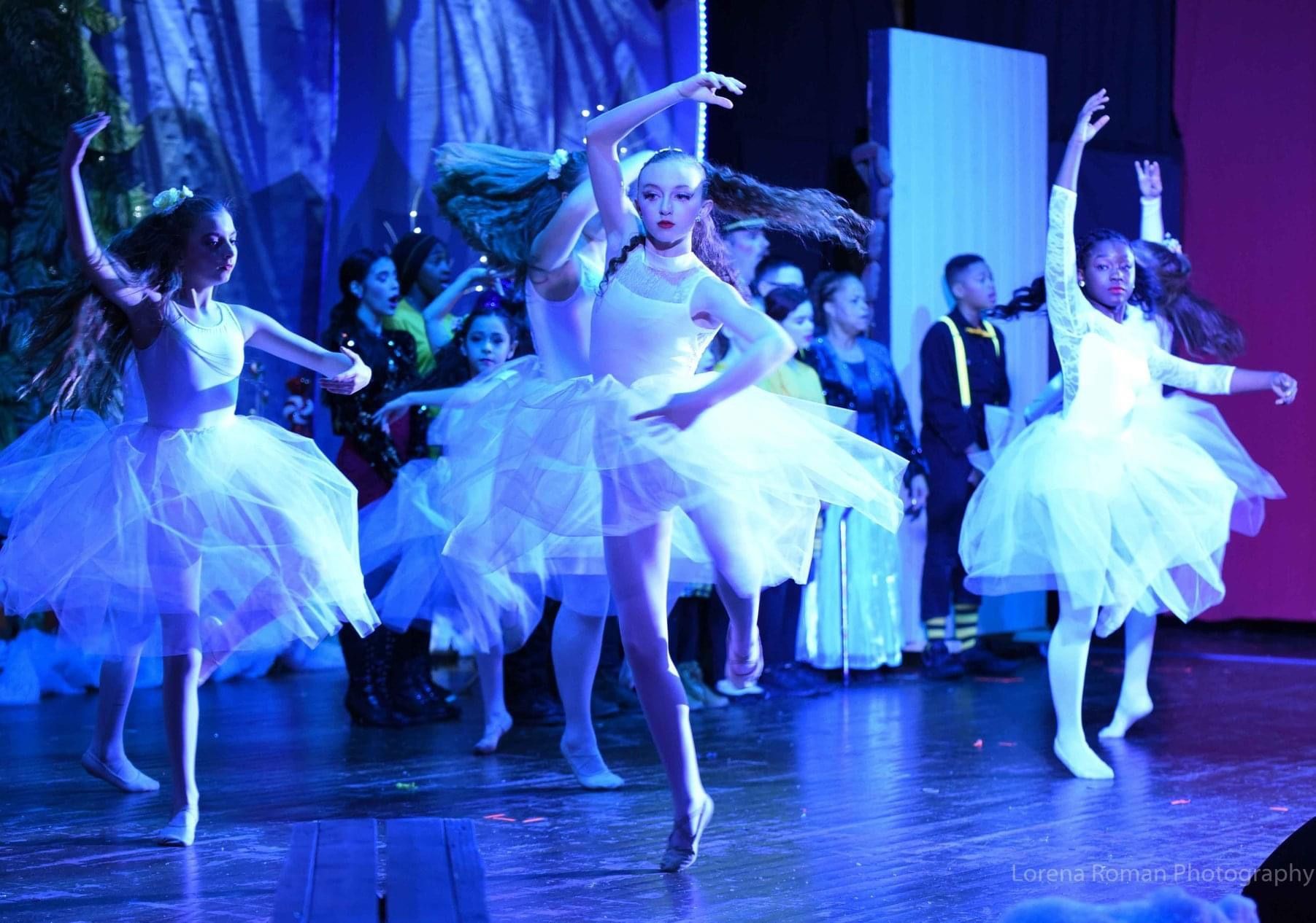 A group of young girls in white tutus are dancing on a stage.
