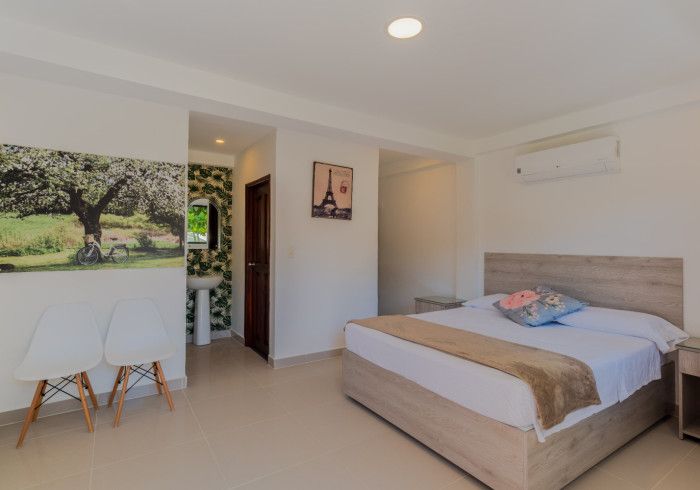 Un dormitorio con una cama, sillas, un lavabo y un cuadro en la pared.