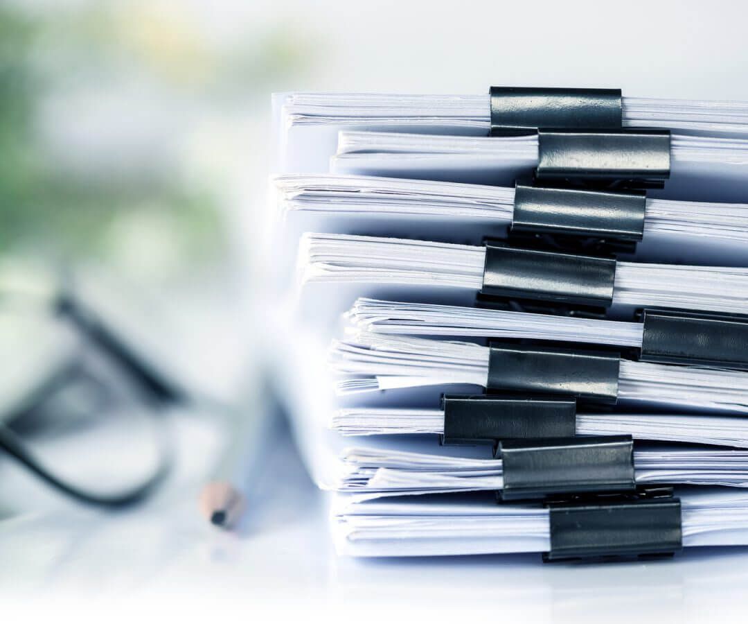 Pile of papers clipped together, glasses and pencil in the background.
