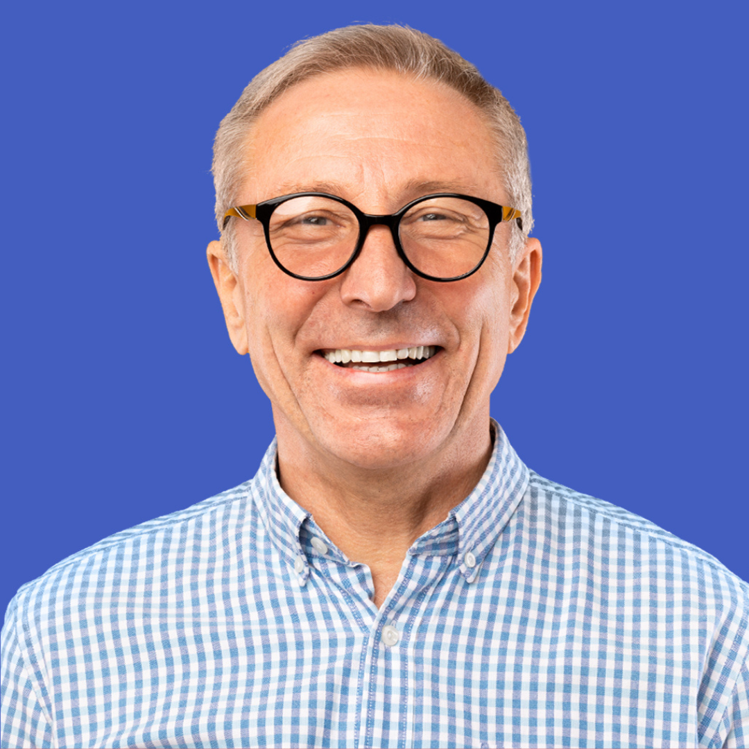 A man wearing glasses and a plaid shirt is smiling.