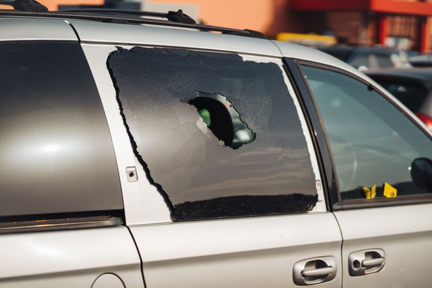 A silver minivan with a broken window is parked in a parking lot.