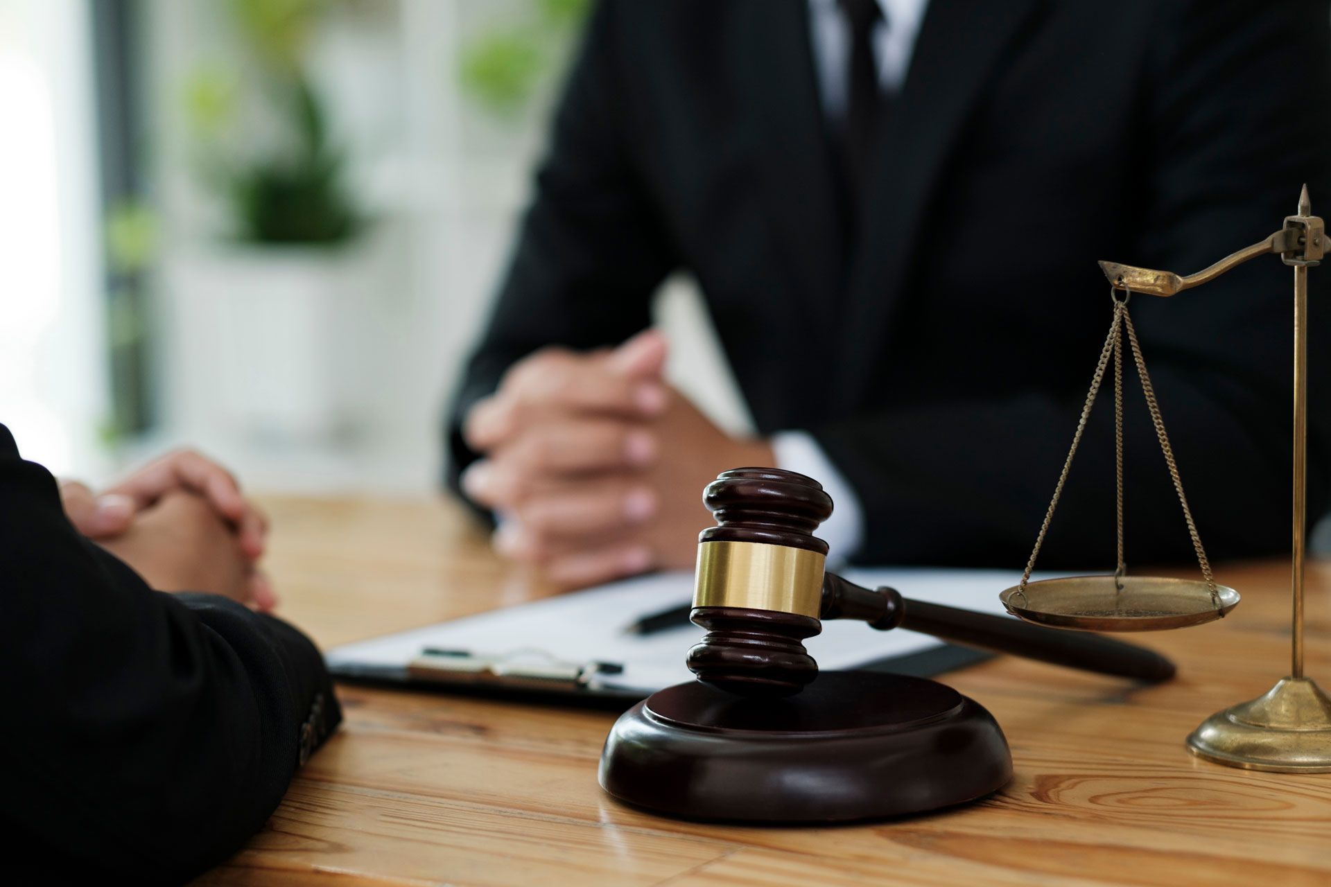 A lawyer in a suit consults with a client, next to a gavel and scales of justice on a wooden desk.