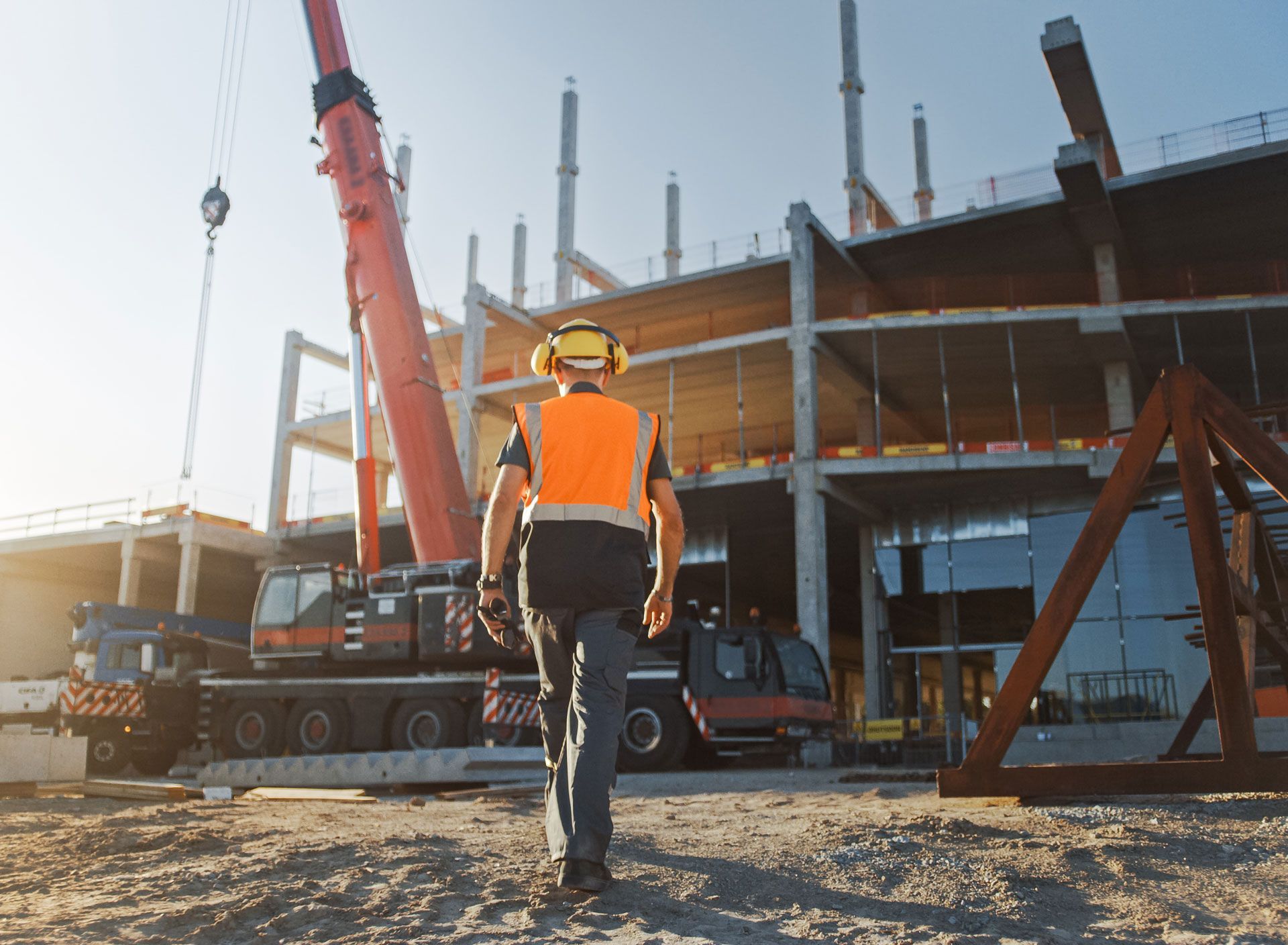 Construction worker in orange vest walks toward building site with crane.