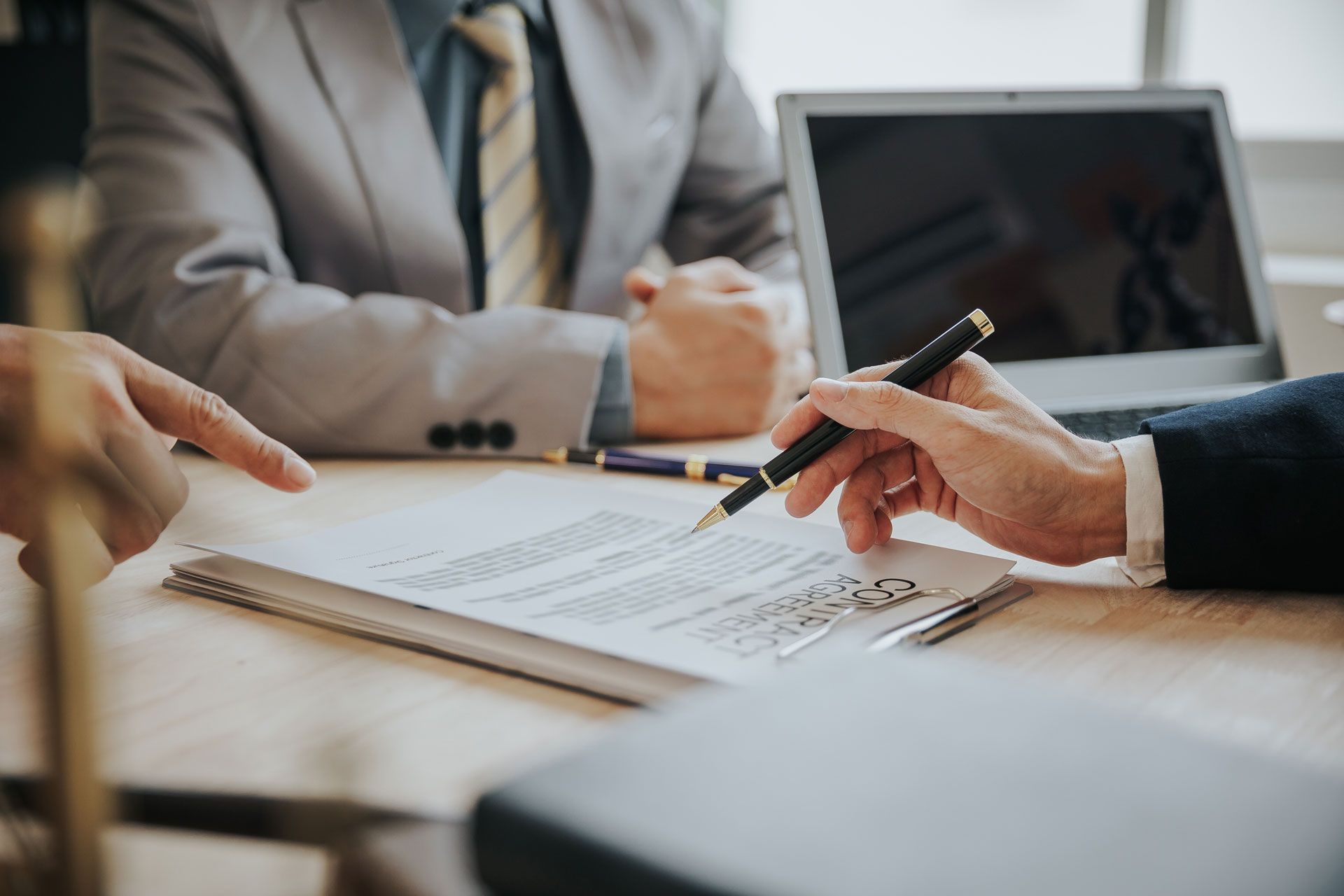 Three business people reviewing a contract with a pen, laptop, and legal book.