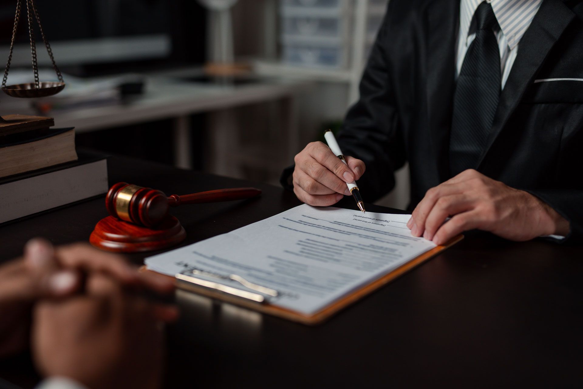 Lawyer signing a document with a client; gavel and scales of justice on desk.
