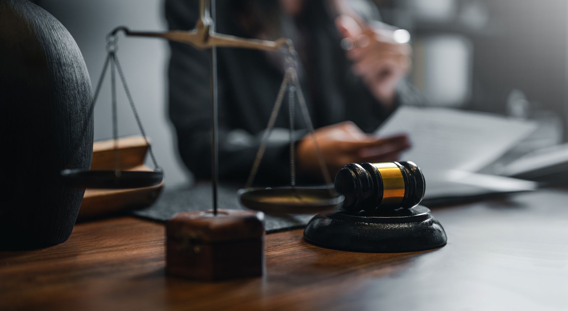 Scales of justice, gavel, and blurred person reviewing documents on a desk.