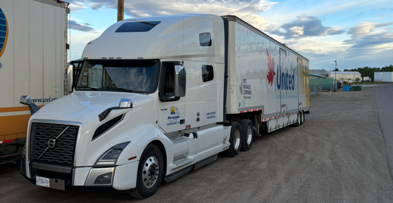 A white semi truck with a trailer attached to it is parked in a parking lot