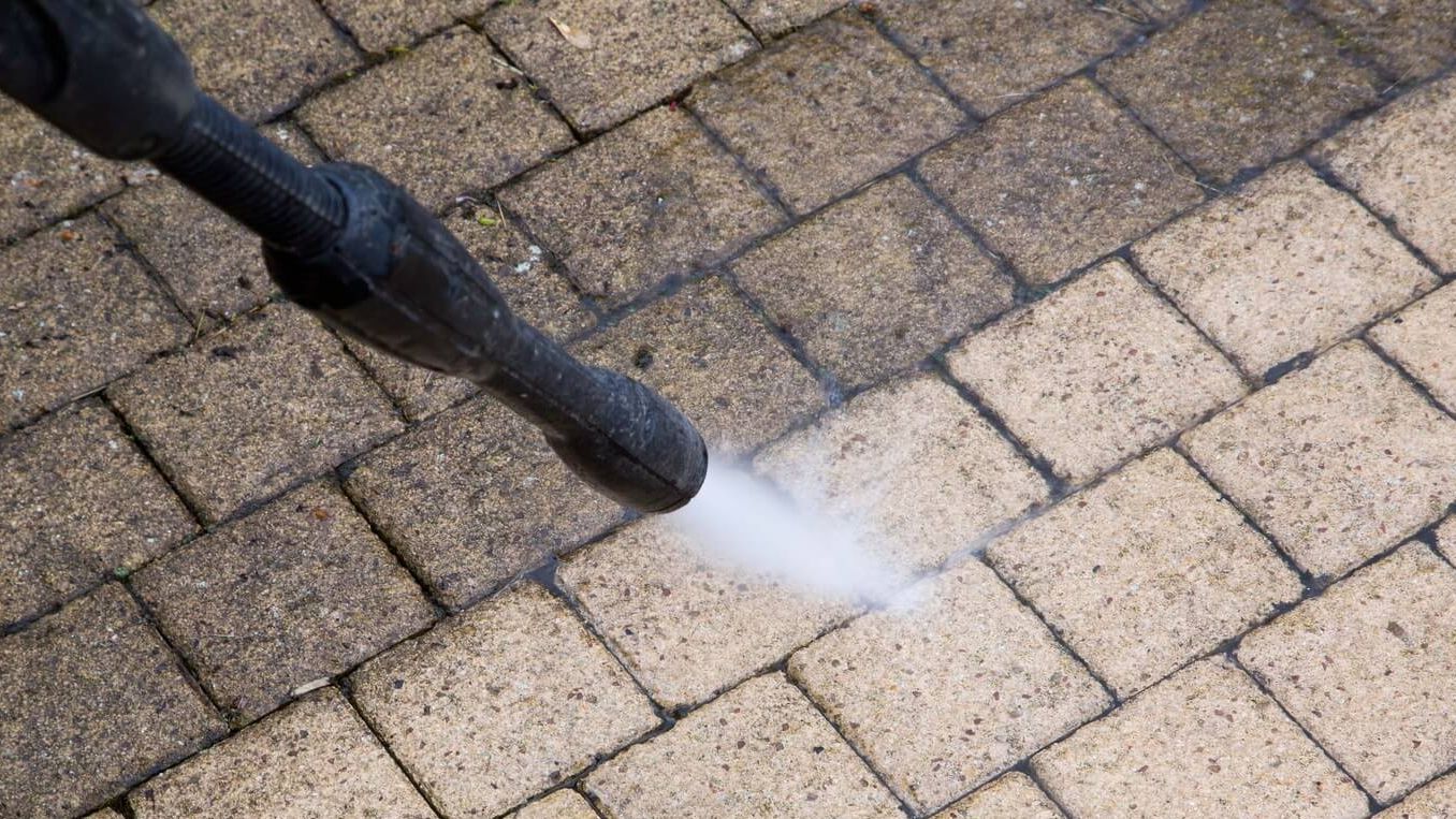 A person is using a high pressure washer to clean a brick walkway.