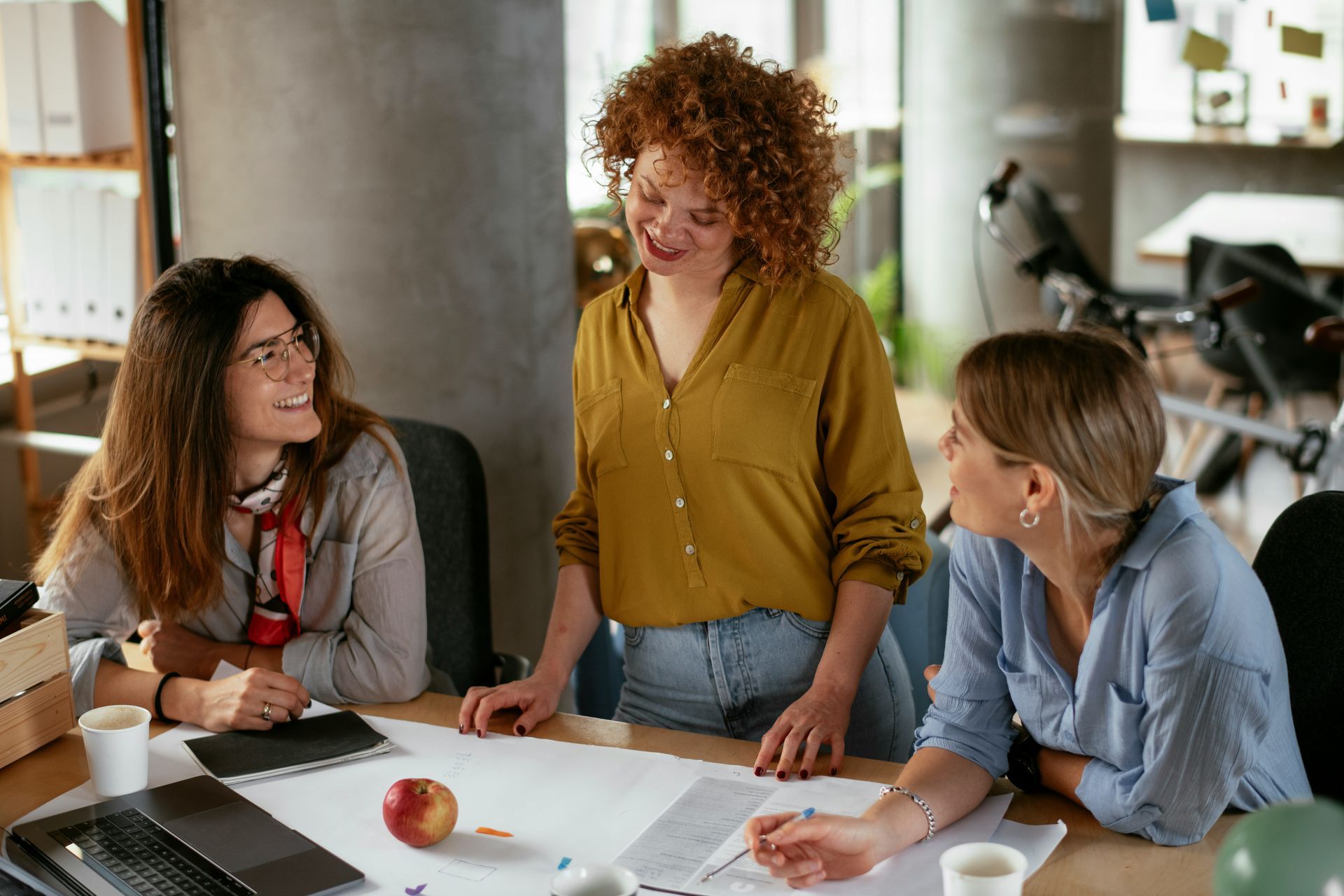 Three women are sitting at a table in an office having a meeting.