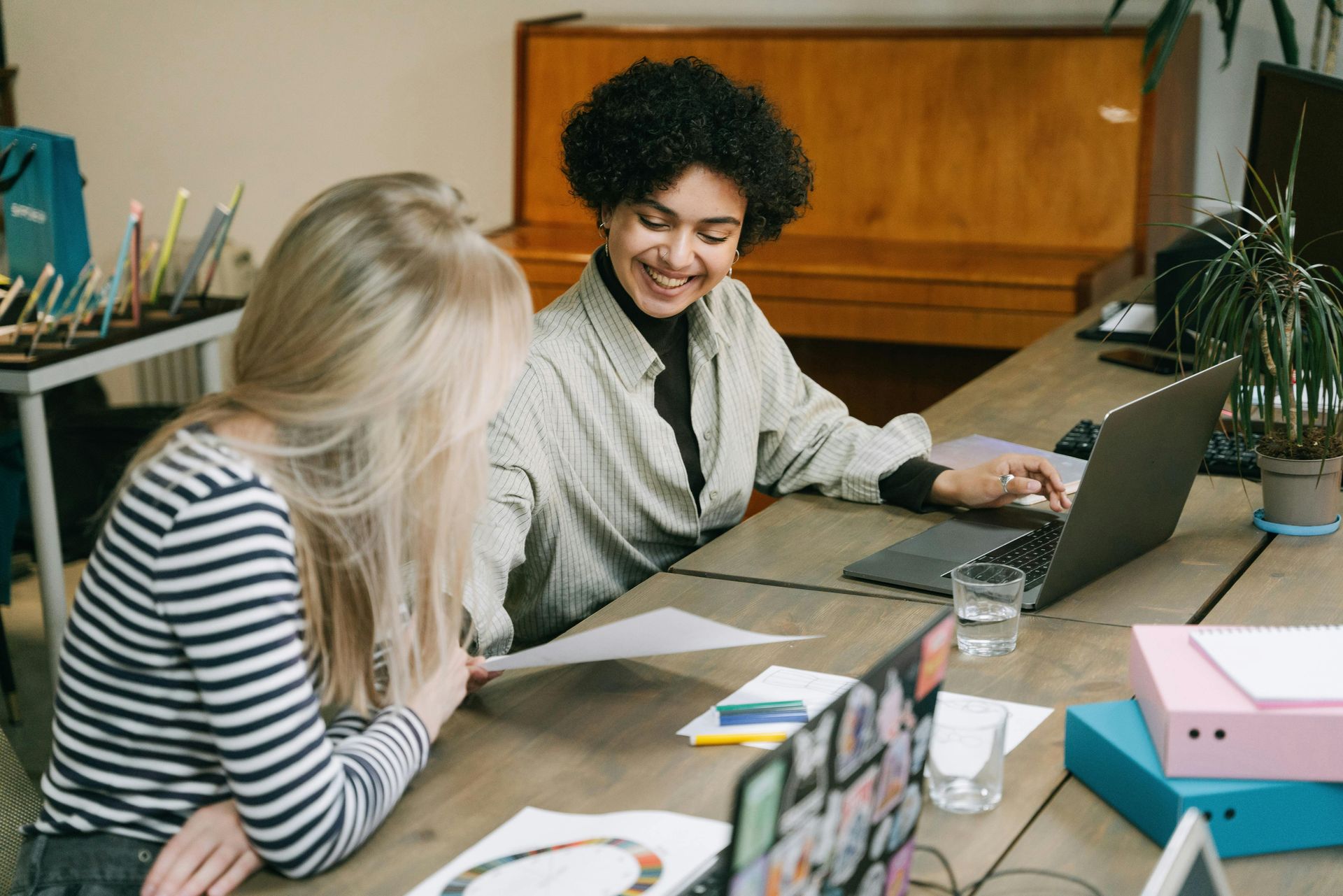 Two women are sitting at a table with a laptop.