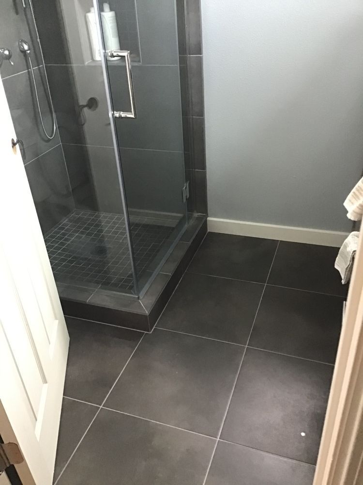 Bathroom with gray tile floor, dark tiled shower, and a glass door. Gray walls.