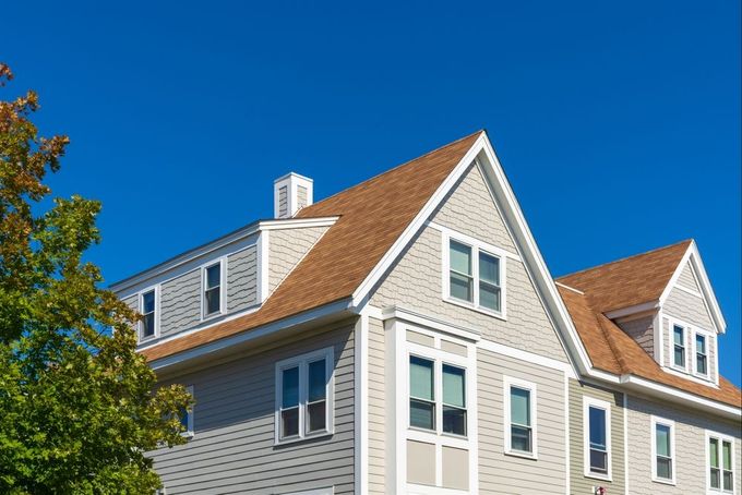 A two-story house with a brown roof and light gray siding against a bright blue sky.