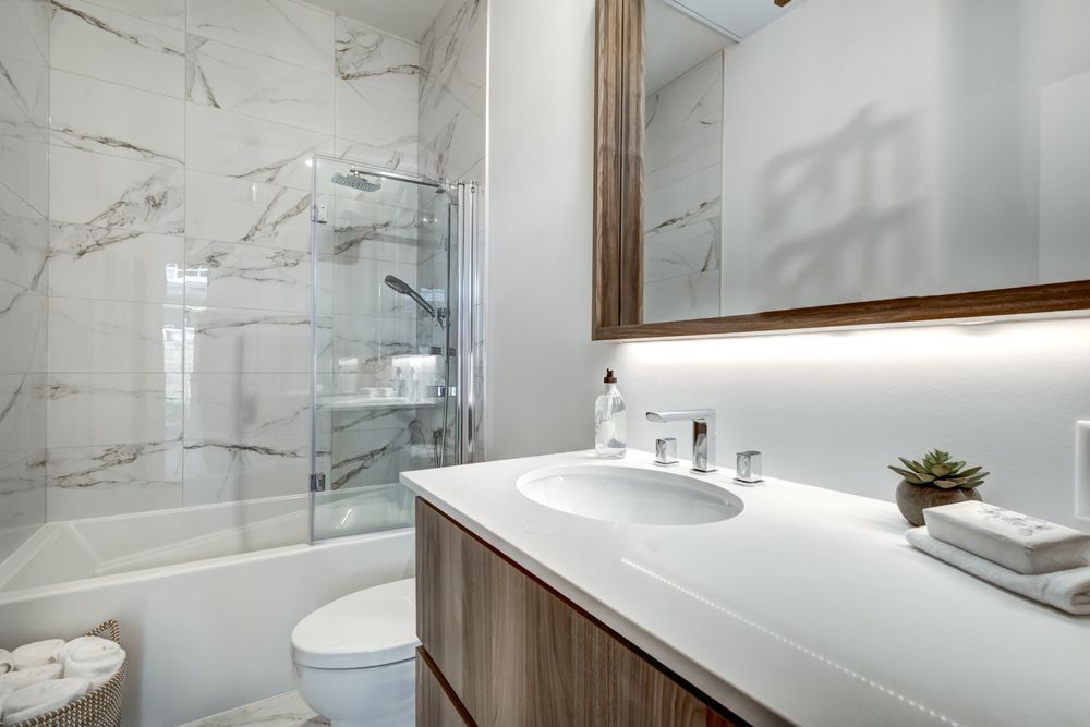 Modern bathroom with marble tile, glass shower, wooden vanity, and large mirror.