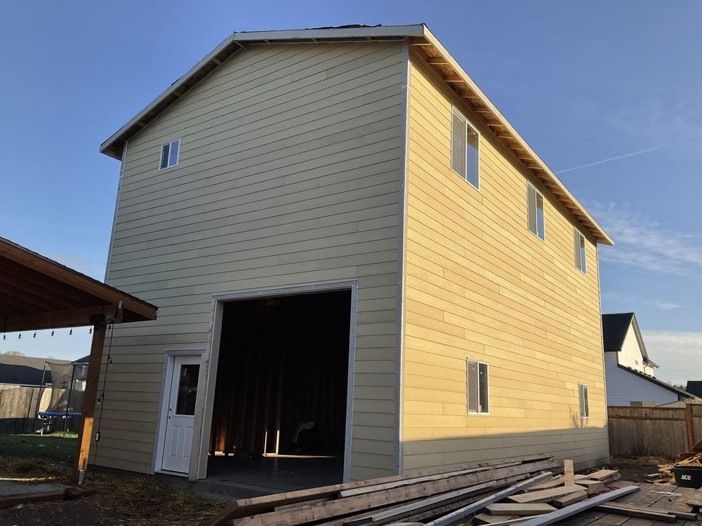 Two-story tan building with large open garage door and small windows, blue sky in background.