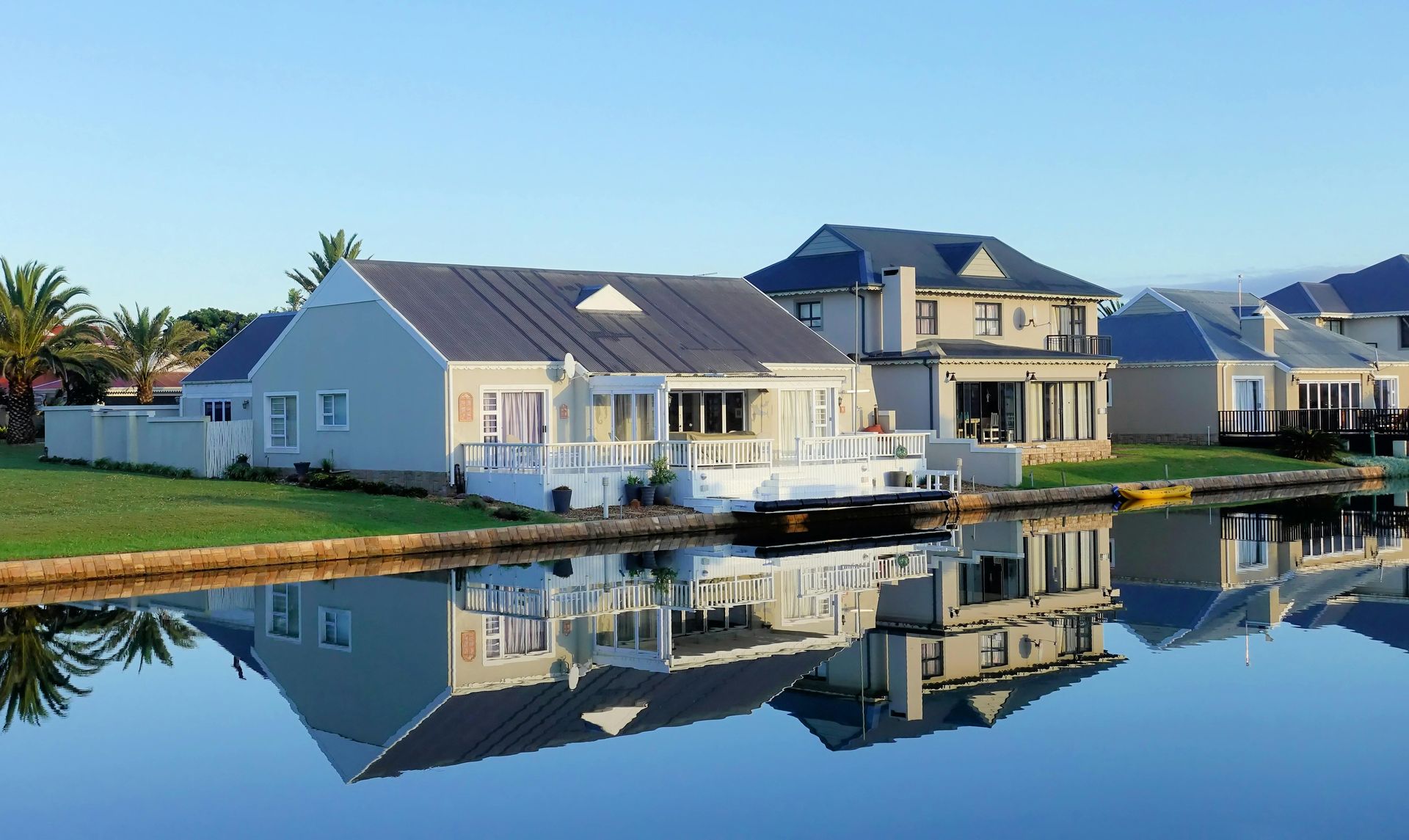 Houses with white trim and gray roofs line a calm canal. Reflections of the homes are in the water.