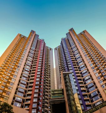 Two tall apartment buildings against a blue sky, with a small building in front.