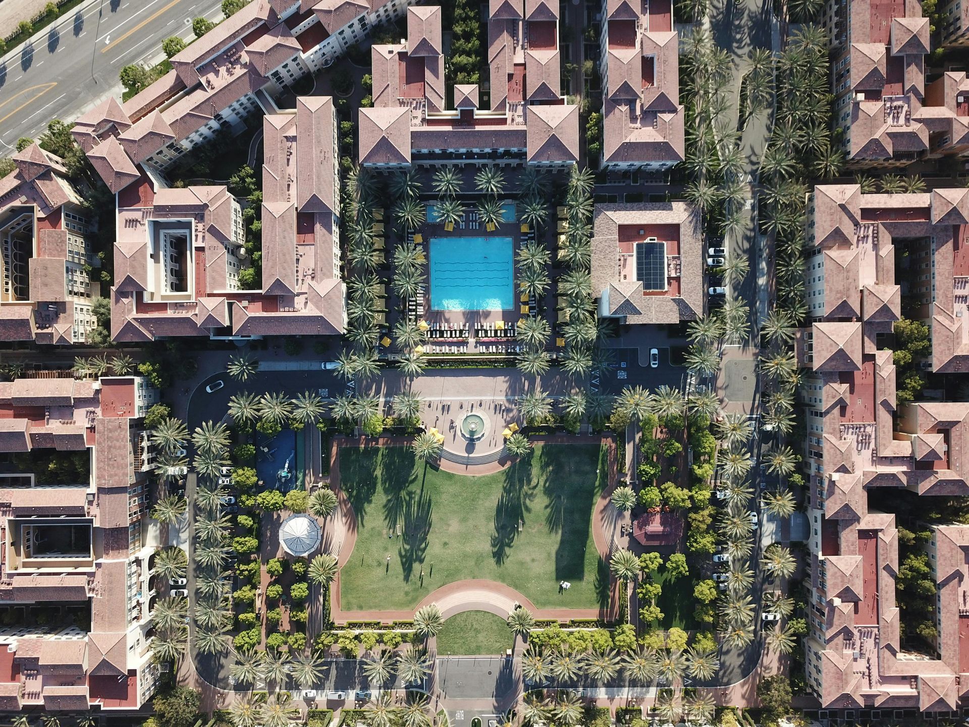Aerial view of a resort with red-tiled roofs, a large pool, green lawns, and surrounding buildings.