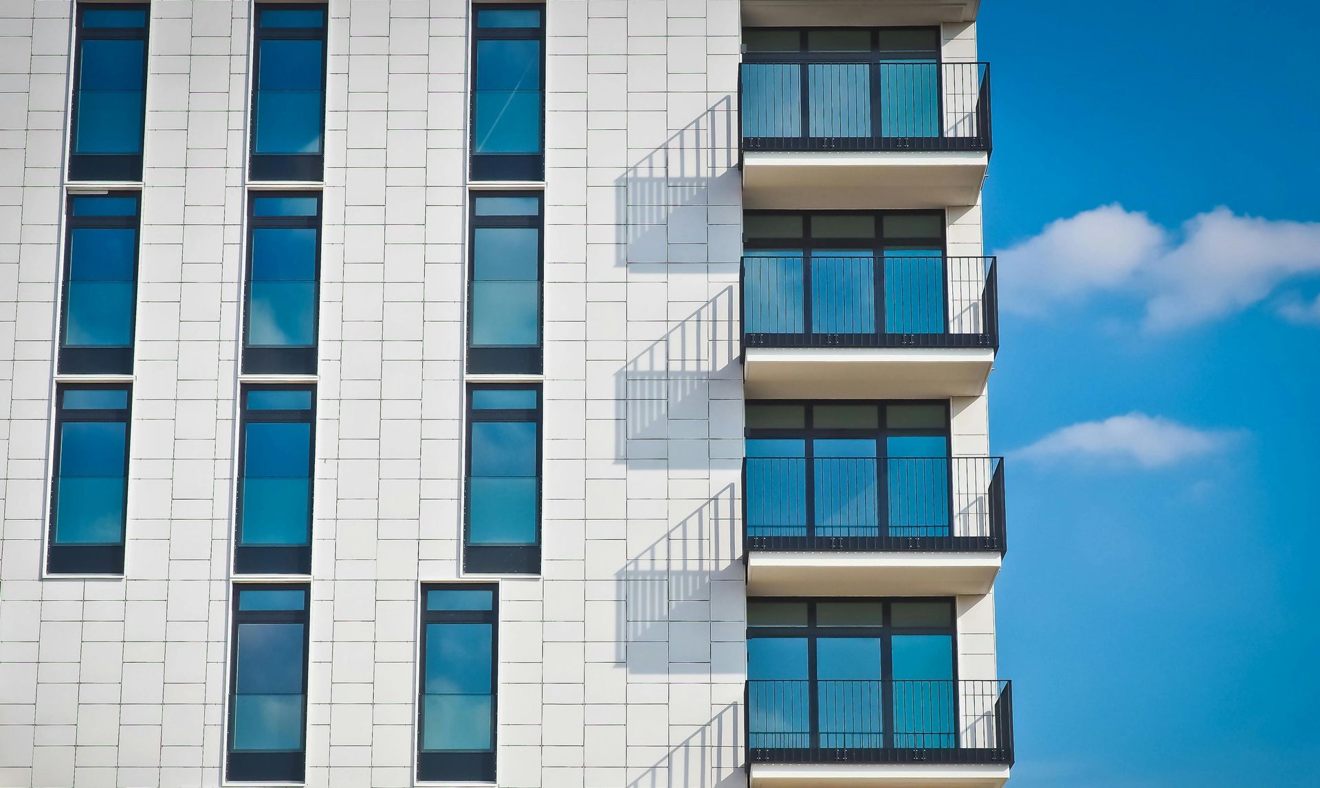 Modern white building with blue windows and balconies against a bright blue sky.