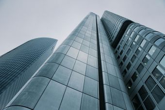 Three modern skyscrapers, silvery-blue, reaching into a cloudy sky.