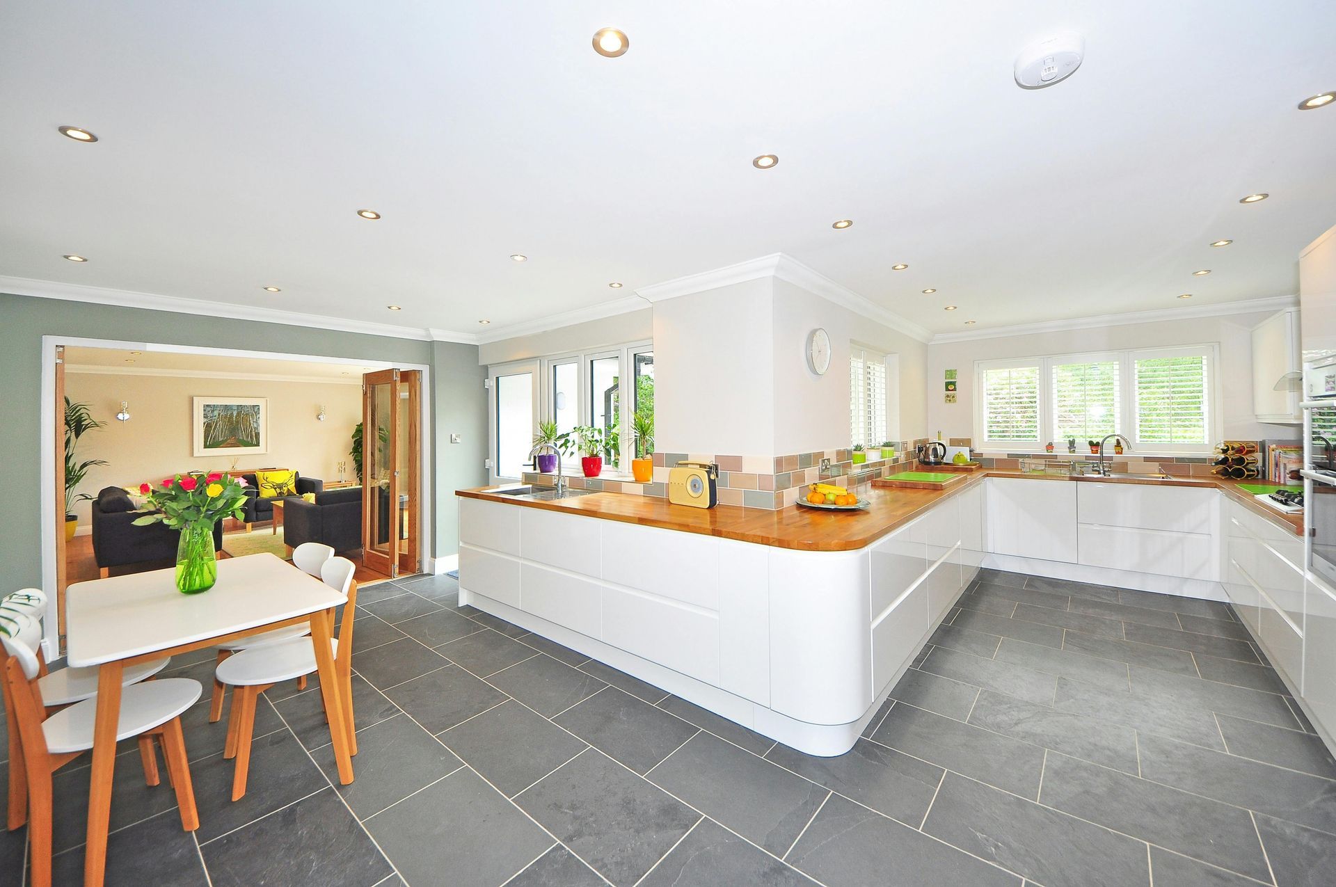 Spacious, modern kitchen with white cabinets, wooden countertops, gray tile floor, and a dining table.