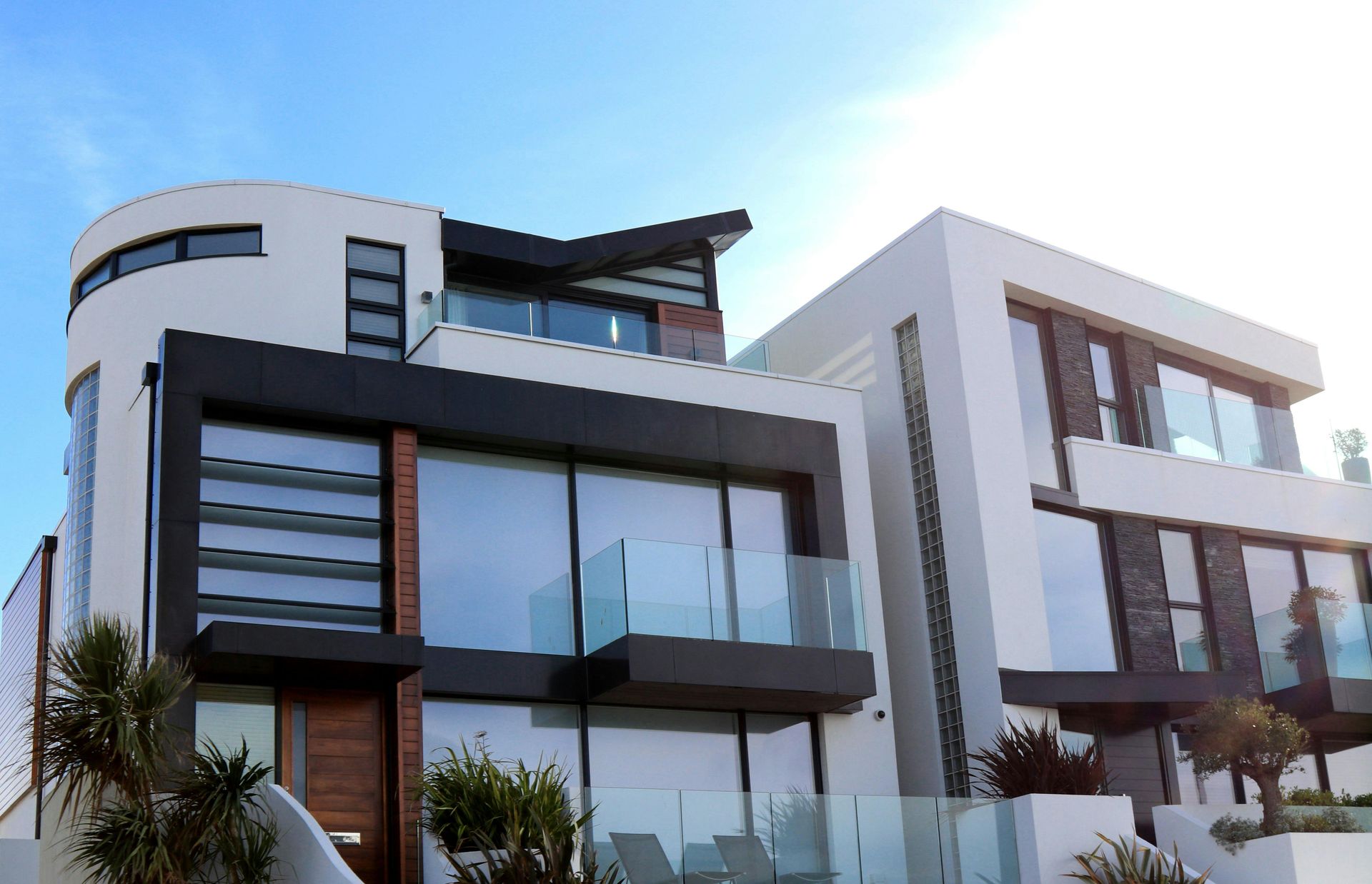 Modern white house with large windows, black trim, and blue sky.