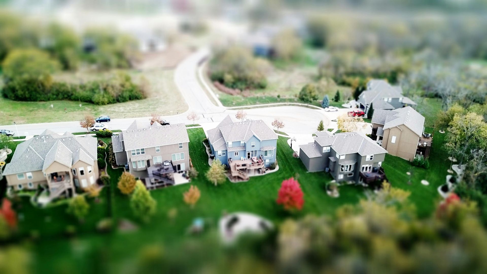 A cluster of houses with green lawns and autumn foliage, with a winding road in a suburban setting.