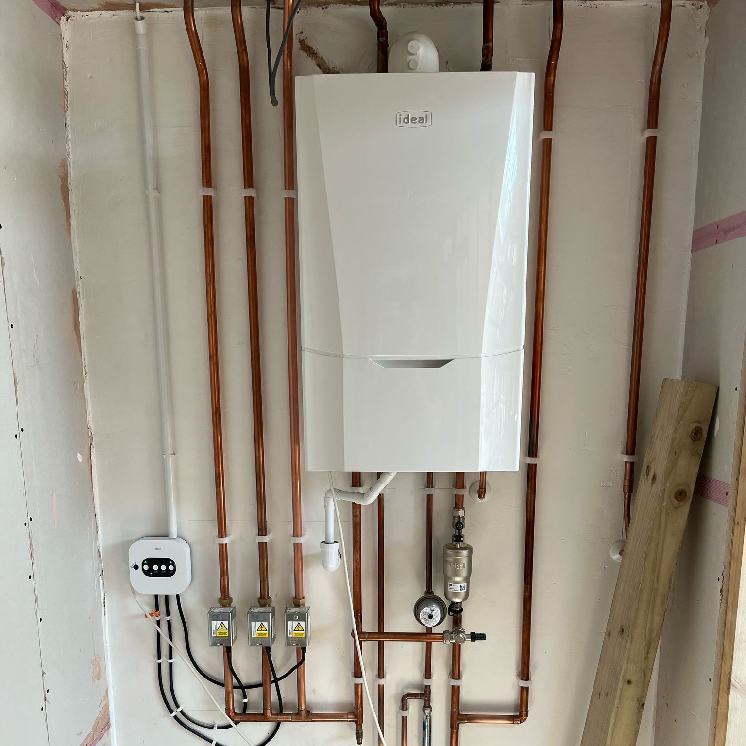 A white boiler is mounted to a wall surrounded by copper pipes.