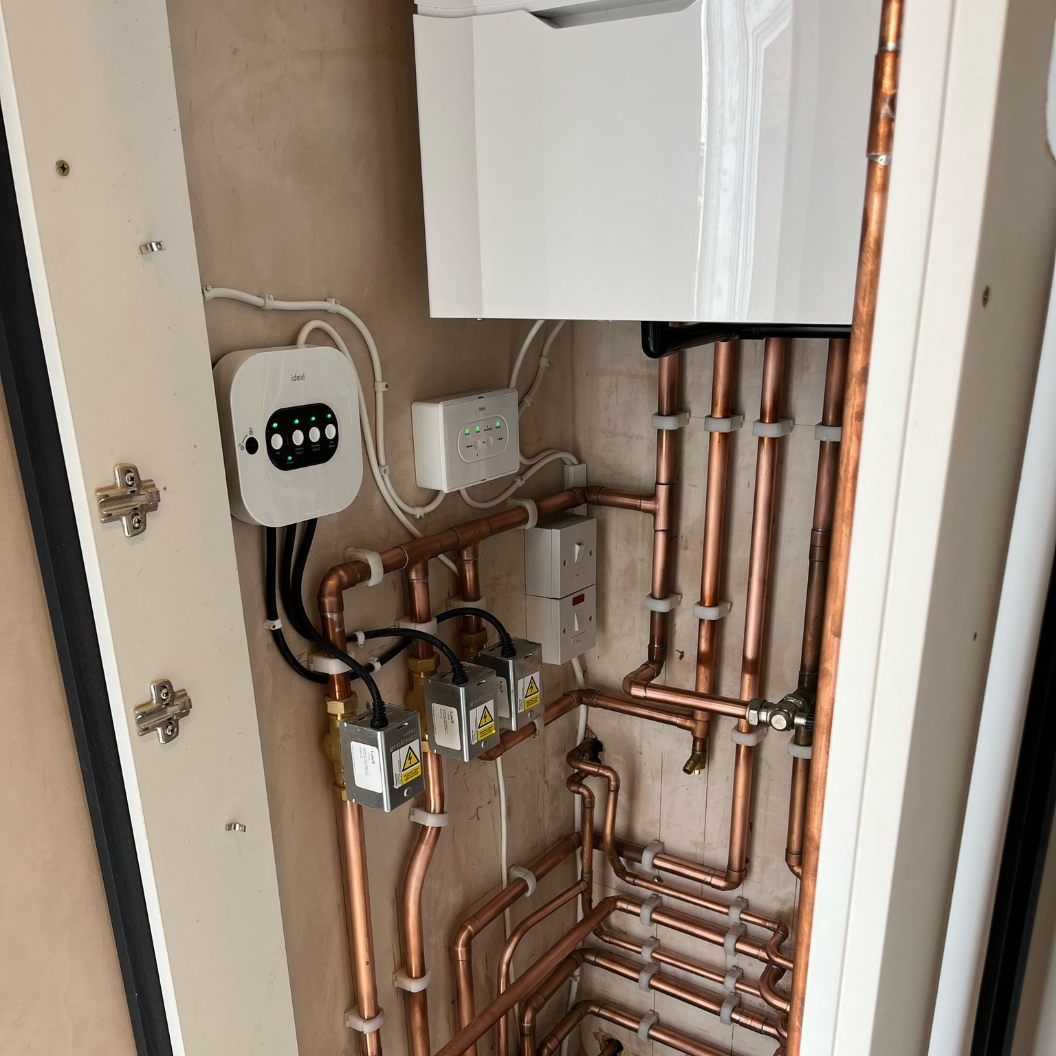 Copper pipes are connected to a white box in a room.