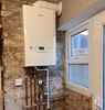 A white boiler is hanging on a brick wall next to a window.