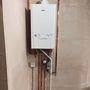 A white boiler is hanging on a wall next to copper pipes.