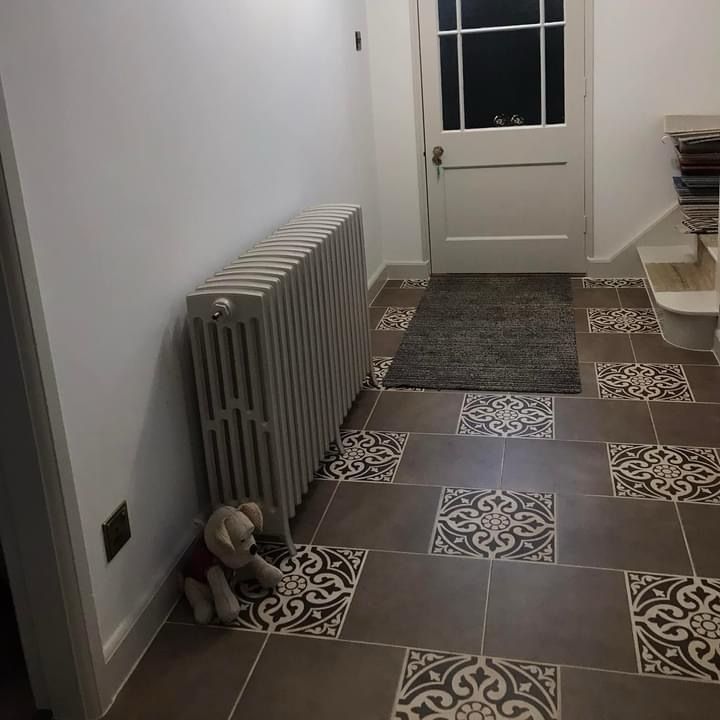 A teddy bear is sitting on the floor in a hallway next to a radiator.