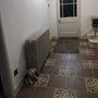 A teddy bear is sitting on the floor in a hallway next to a radiator.