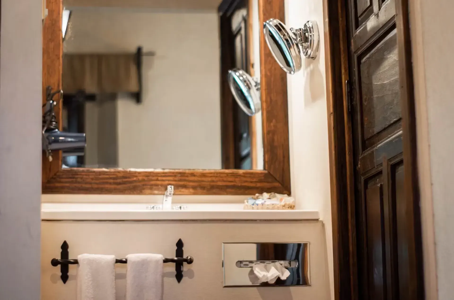 Bathroom with a wooden-framed mirror, two silver shower heads, towels on a black rack, and a decorative door.