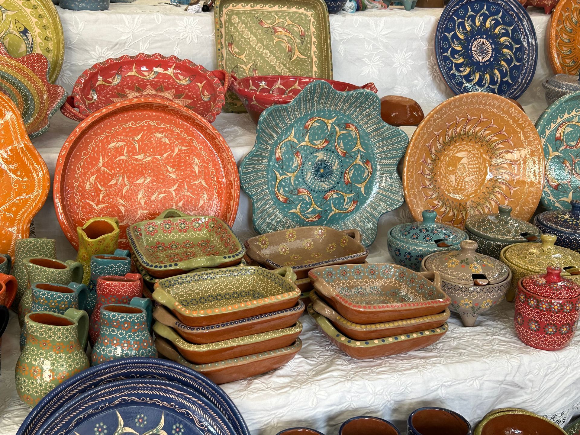 A display of colorful, intricately patterned ceramic plates and bowls on a white cloth.